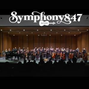 Symphony847 orchestra musicians standing on stage at Libertyville High School at their March 1, 2025 concert and receiving a standing ovation from the audience who can also be seen in this photo.