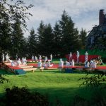 Gallery 5 - Looking through trees to a green lawn, red and blue platforms are used by people as a band performs.